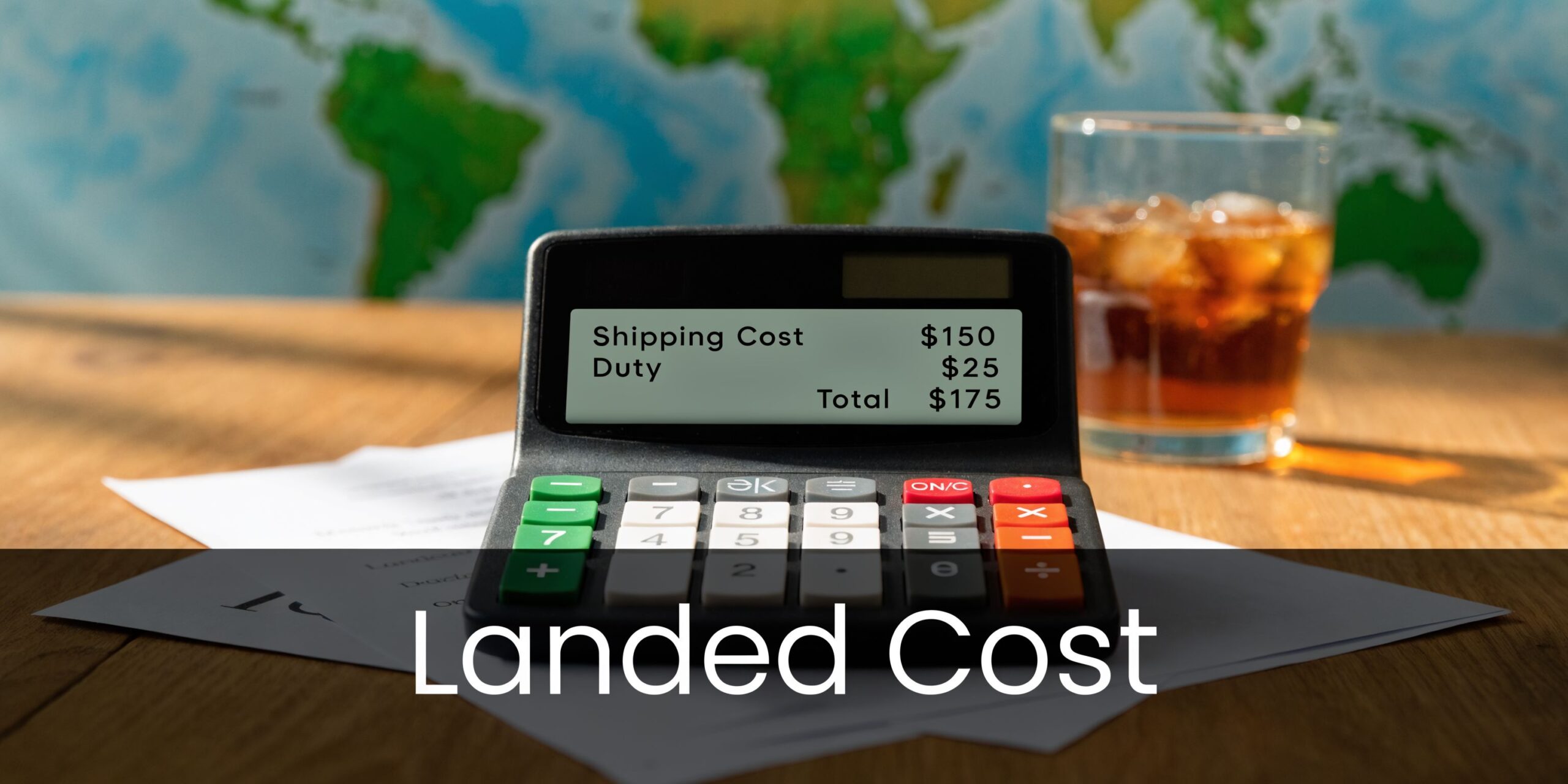 A calculator displaying landed cost components like shipping and duty fees on a wooden desk with a drink.